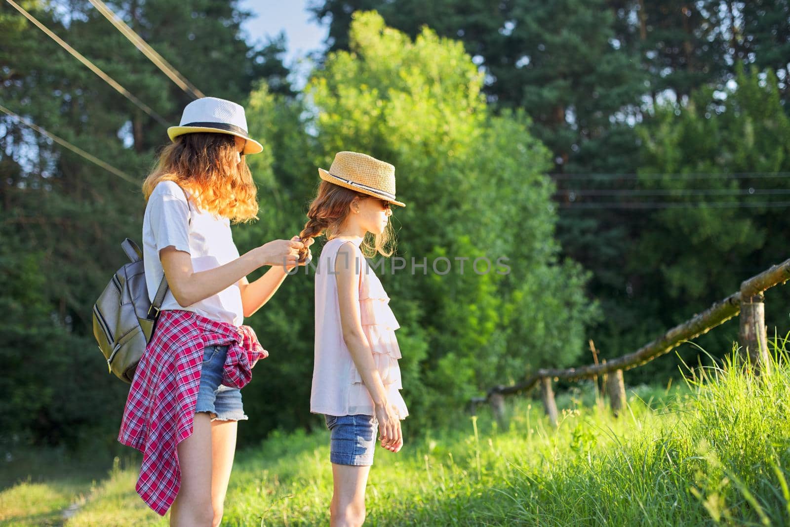Summer, happy kids walking enjoying nature vacation, older sister braids her younger hair.