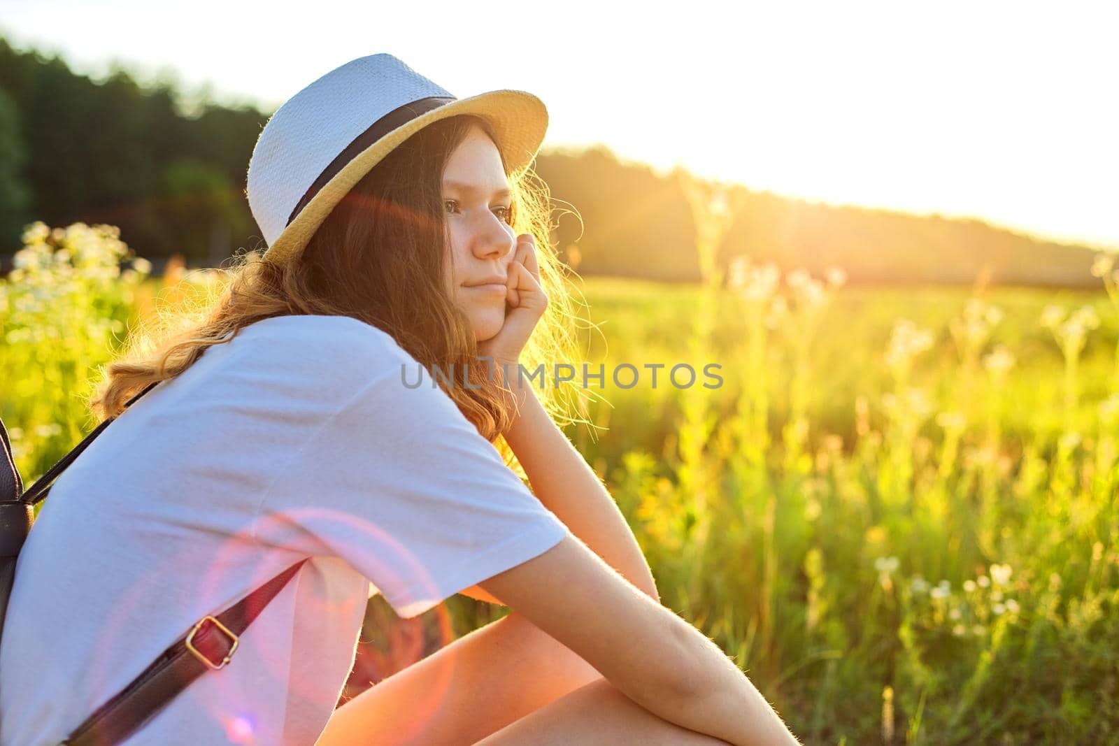 Happy teenager girl in hat with backpack sitting on country road, enjoying summer vacation by VH-studio