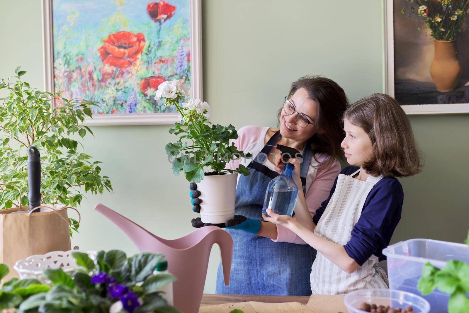 Mother and daughter kid care together for house flower in pot, girl sprinkles spray on plant by VH-studio