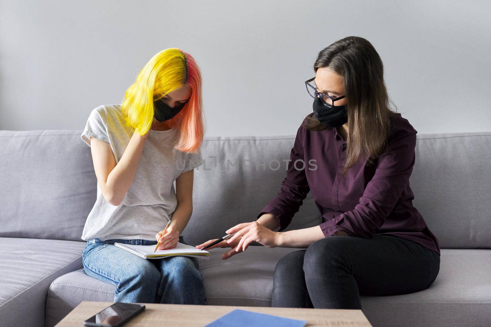 Teacher working with college student individually, woman and teenage girl in black protective masks. Virus prevention, health protection, education concept