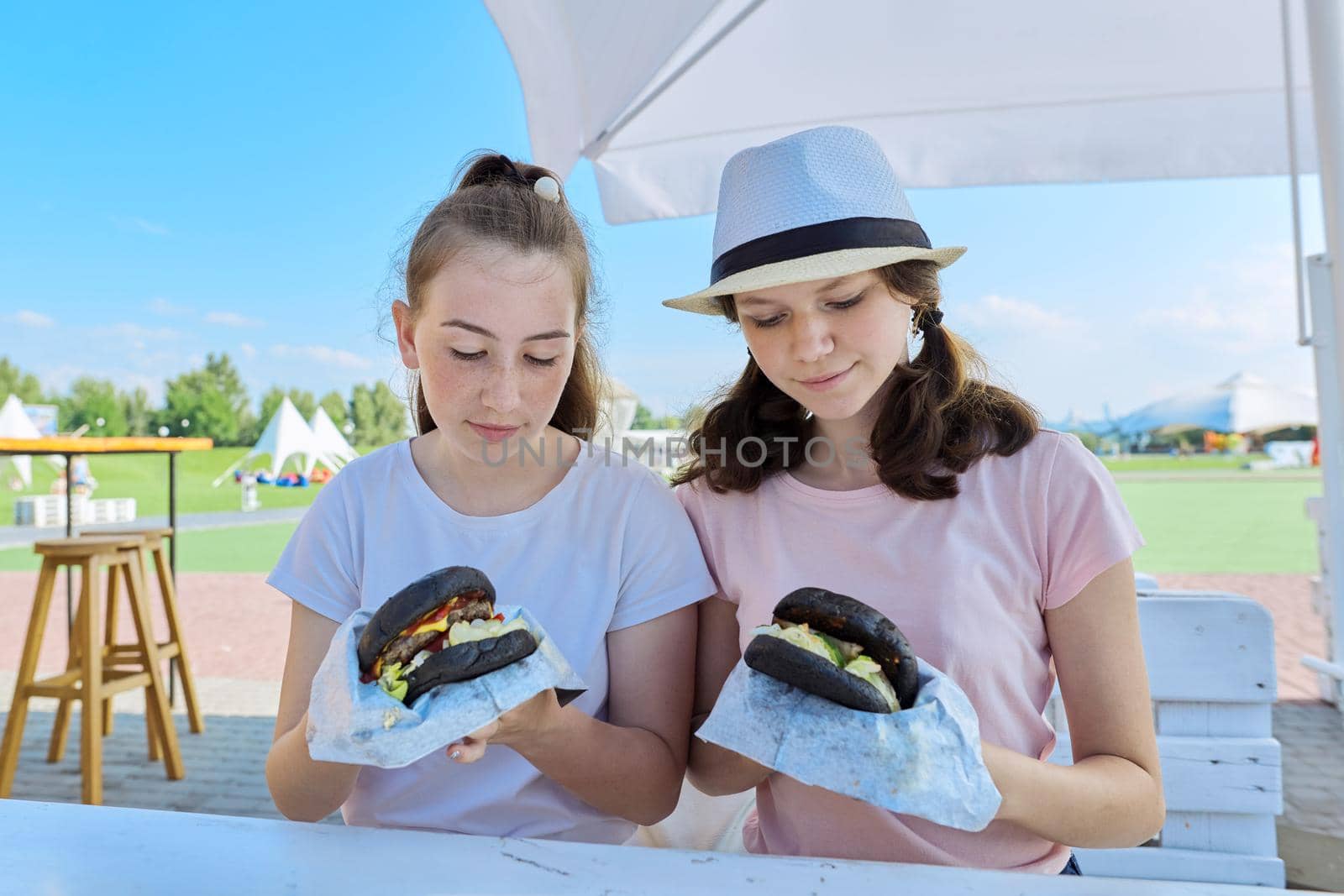 Teens two girls friends eating black burgers fast food, street food.