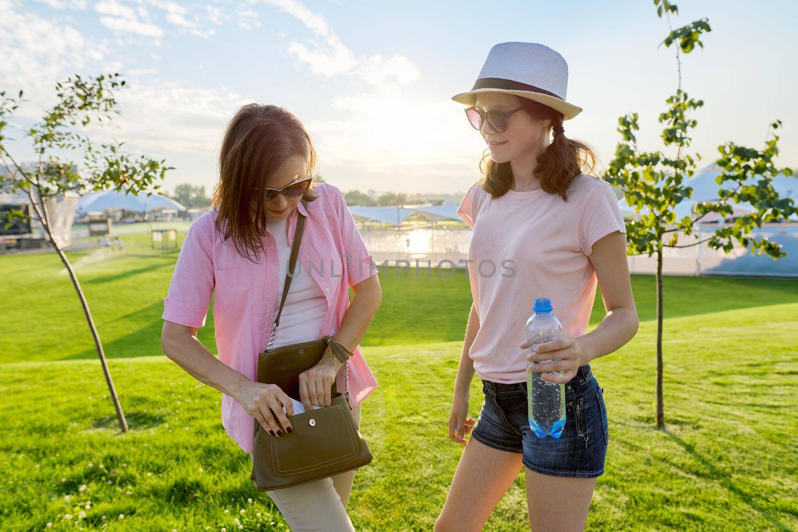 Mother and teenage daughter walking together, mom with bag girl with bottle of water, family lifestyle concept