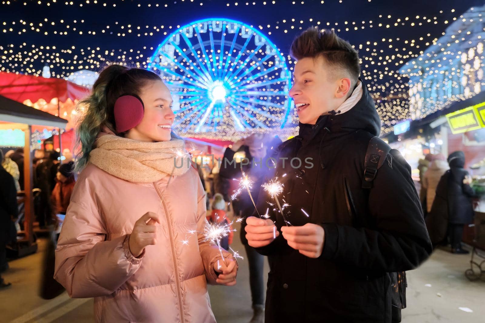 Happy teenage couple with sparklers celebrating and having fun at Christmas market by VH-studio