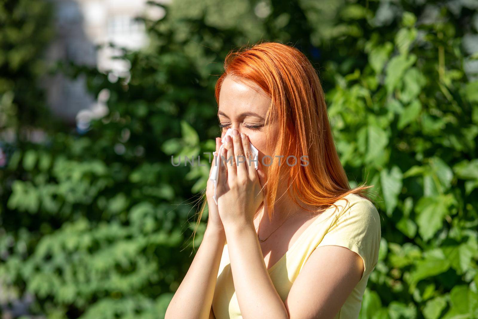 Young redhair woman sneezing in park. Pollen Allergy symptoms by adamr