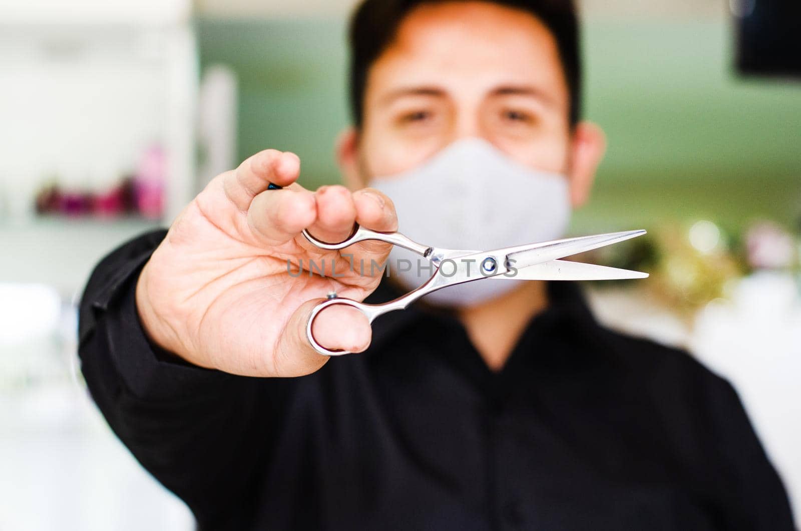 Portrait of an attractive barber, guy with safety mask, holding scissors in his hand, social distancing, preventive measures against the virus in pandemic