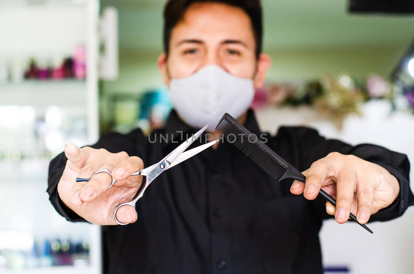 Portrait of an attractive barber, guy with safety mask, holding scissors and a comb in his hands, social distancing, preventive measures against the virus in pandemic. by Peruphotoart