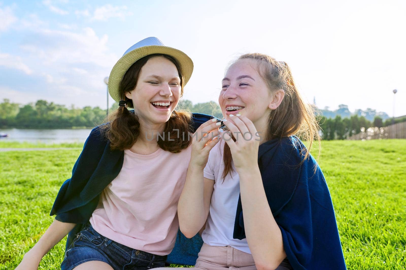 Girlfriends teenagers having fun while sitting on the grass on a sunny summer day, friendship adolescence vacation concept