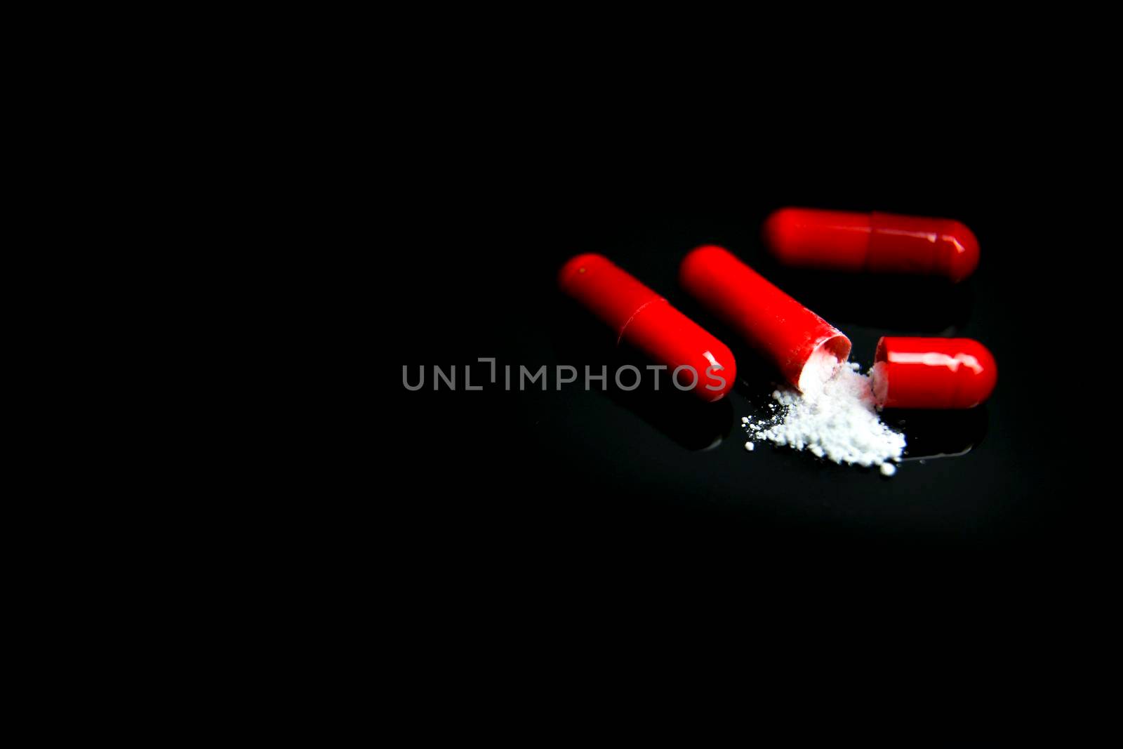 Open Red capsule with white medicine on black background