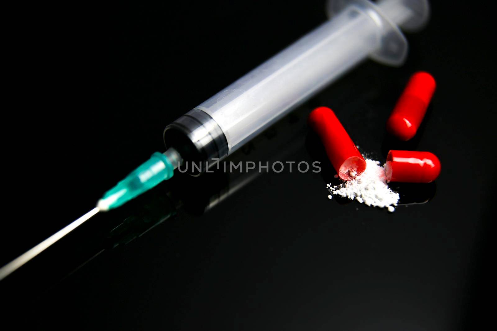 Open Red capsule with white medicine next to syringe on black background