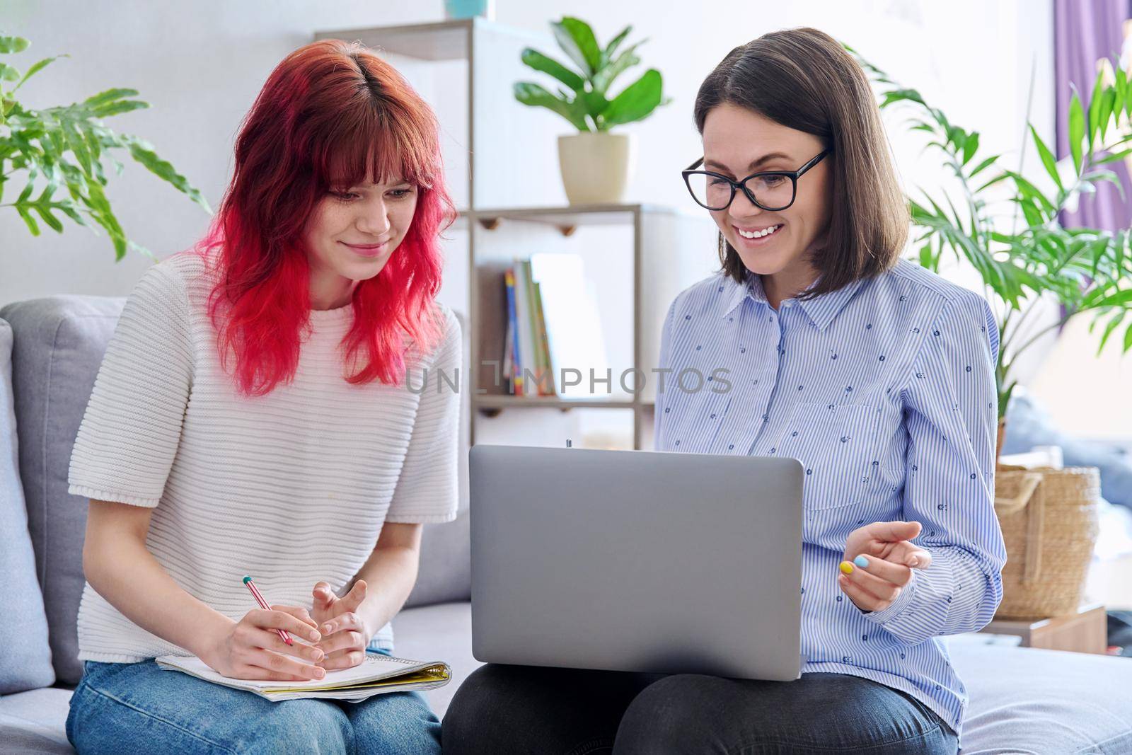 Female teacher teaches student teenage girl, sitting together on couch in office, educational counseling, using laptop. Education, knowledge, individual training, adolescence concept