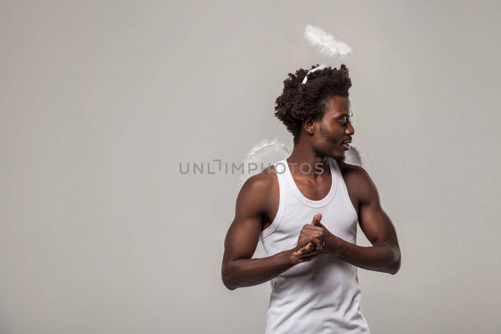 thoughtful confused man. dark skinned angel with nimbus and winks standing with raised arm and profile side thinking and looking. studio shot, Indoor, isolated on gray background