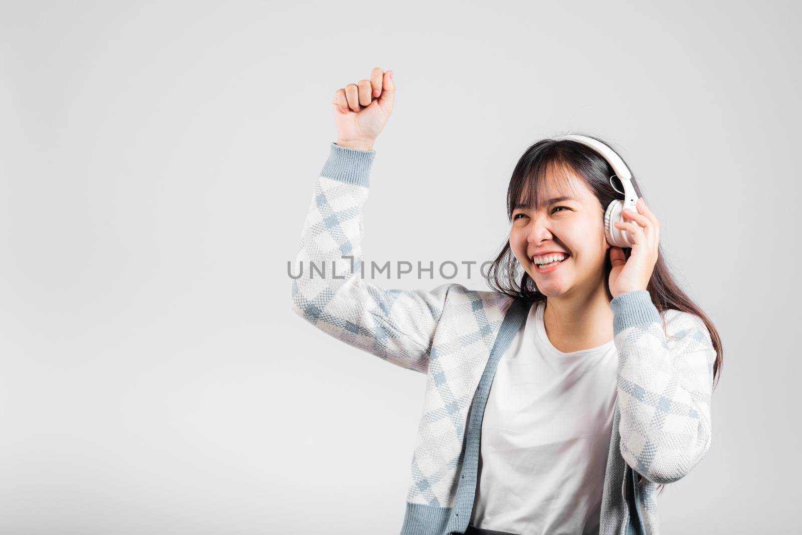 Woman excited smiling listening to music radio in bluetooth headphones and dancing with smartphone studio shot isolated white background, happy Asian young female Karaoke online app in mobile phone