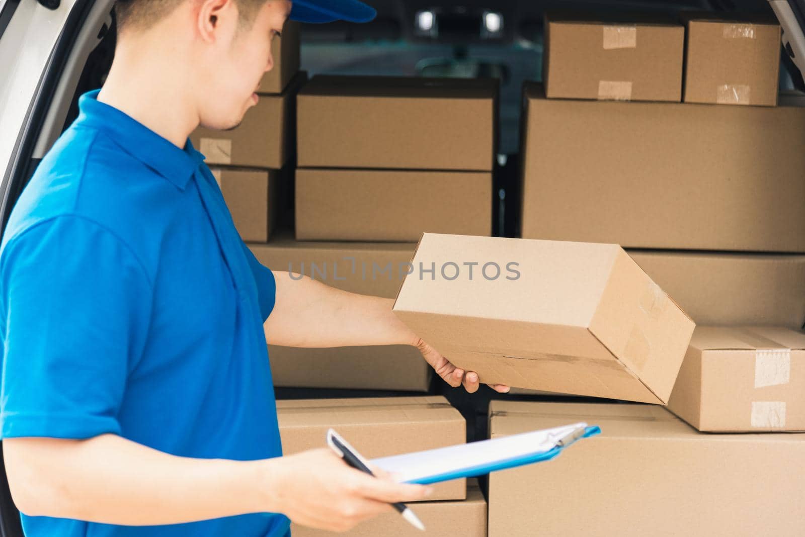 Asian young delivery man courier in uniform hold documents clipboard checking list parcel post boxes near a car for service shipment to customer, Online shopping service concepts
