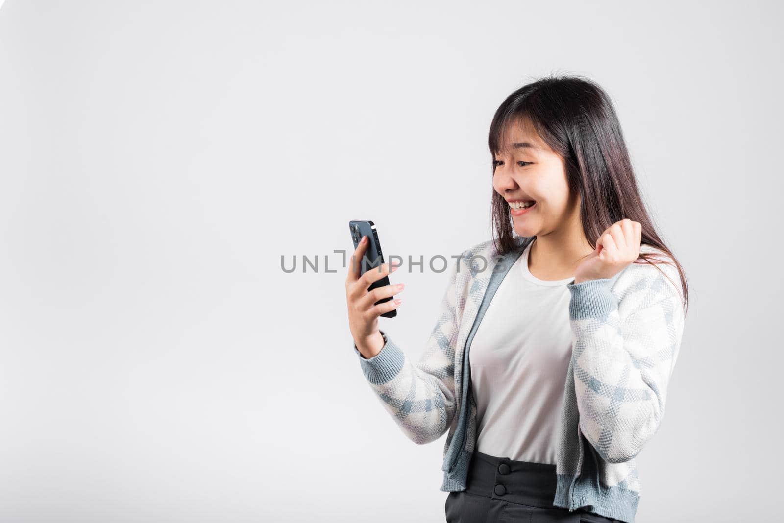 Woman excited holding mobile phone funky successful raise fists say yes by Sorapop