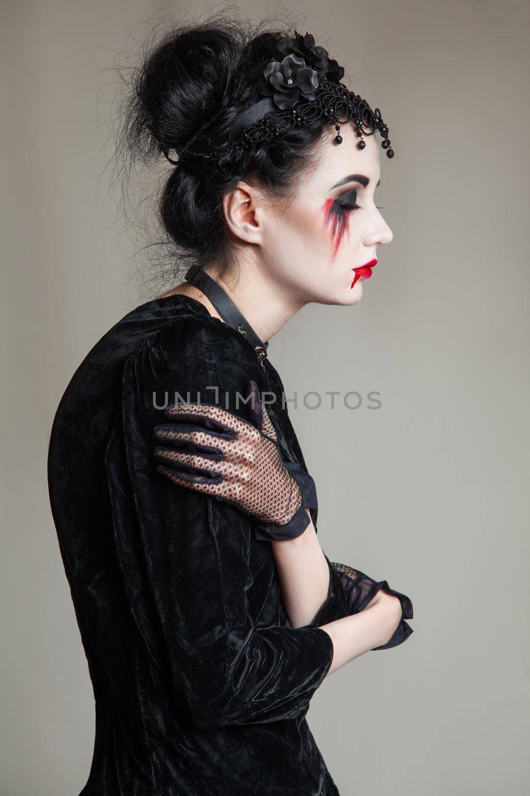 Young beautiful gothic woman with white skin and red lips with bloody drops wearing black collar with spikes. Red smokey eyes. Halloween makeup. by Khosro1