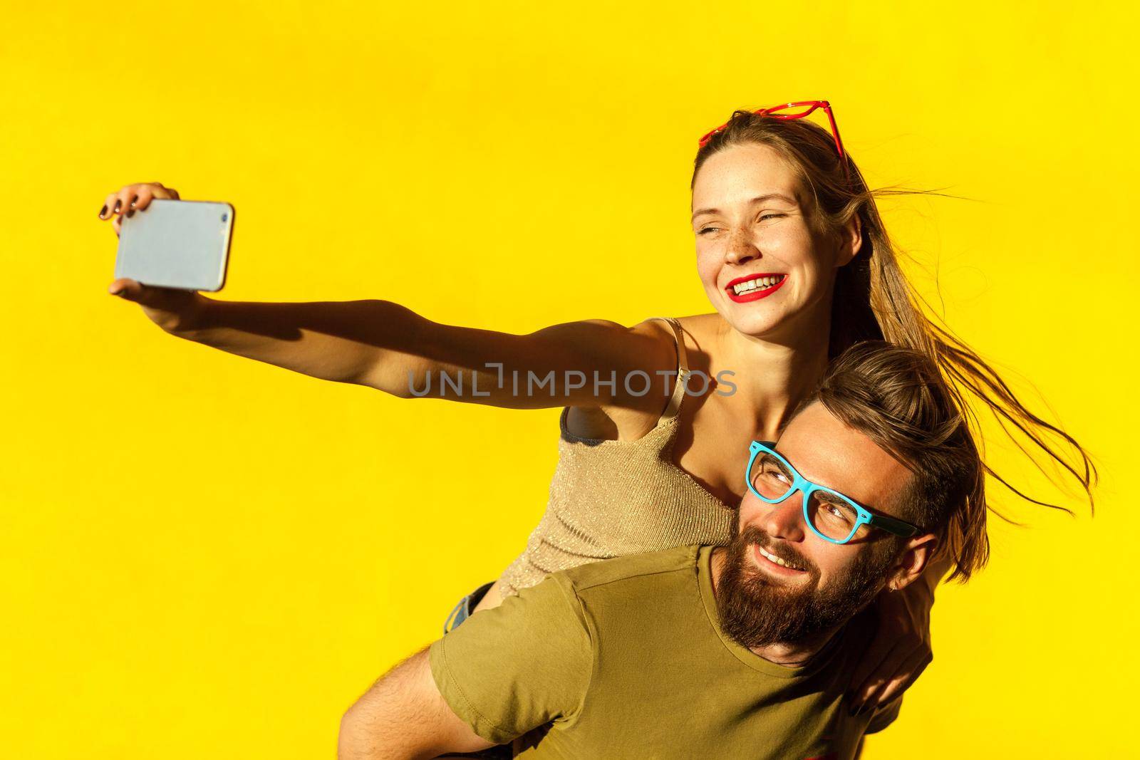Happiness couple. Piggyback. Selfie. Hipsters couple macking selfie on yellow background. Studio shot