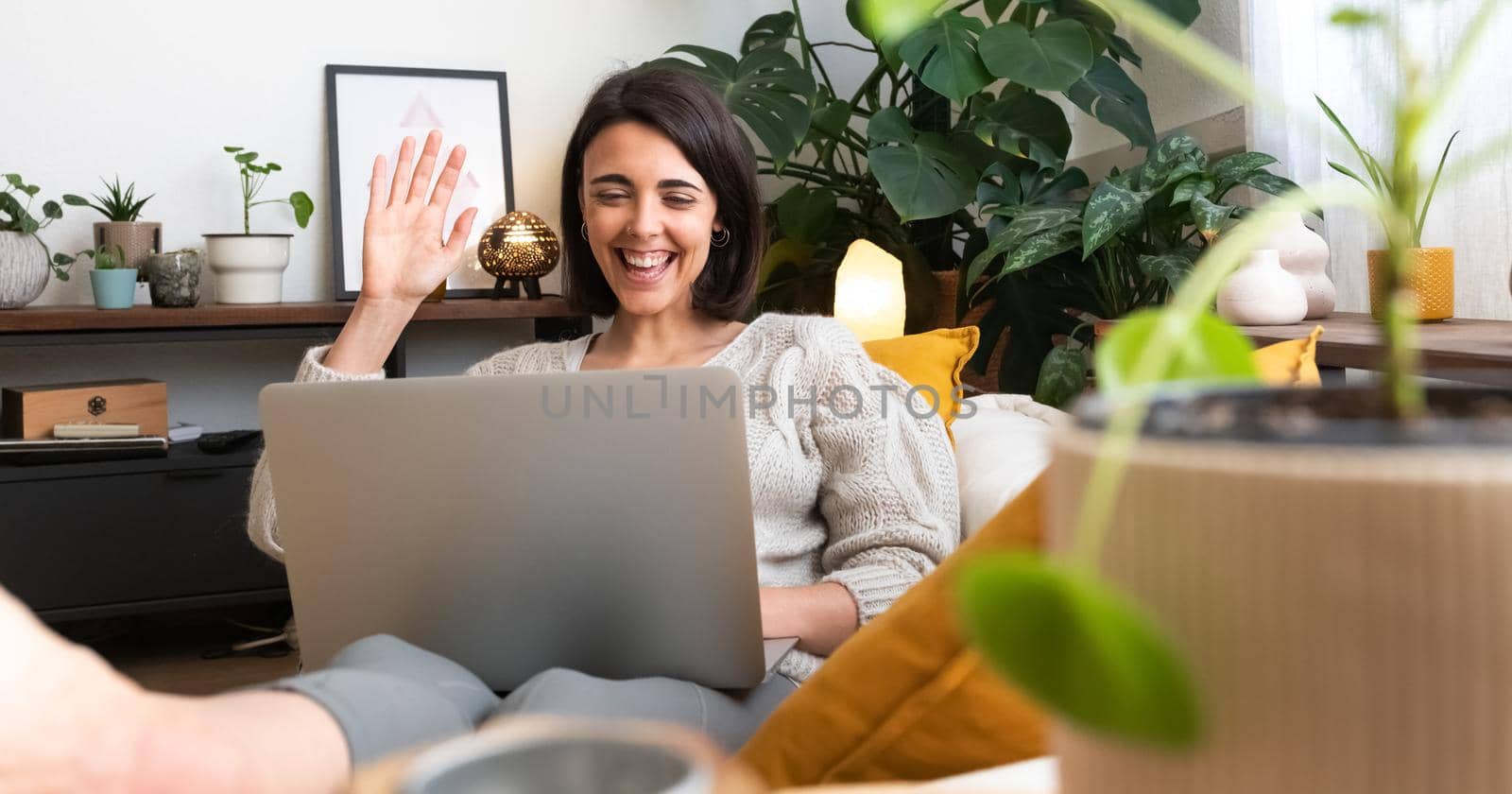 Panoramic image of young happy caucasian woman waving hand hello during online video call at home cozy living room. Technology concept.