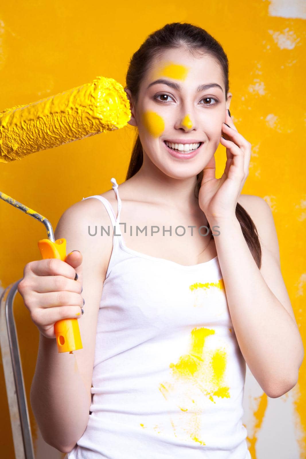 Beautiful young caucasian model in coloured shorts and white shirt and posing holding outrigger in her hands, painting the wall and looking at camera. Studio shot.