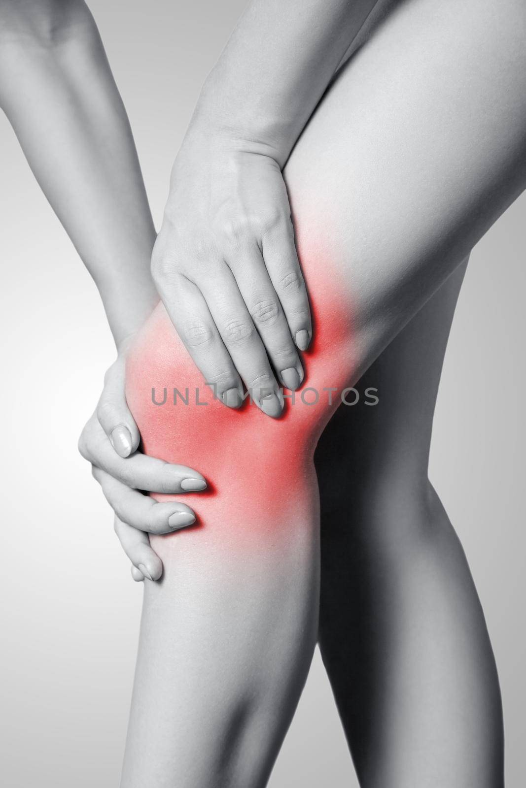 Closeup view of a young woman with knee pain on gray background. Black and white photo with red dot.