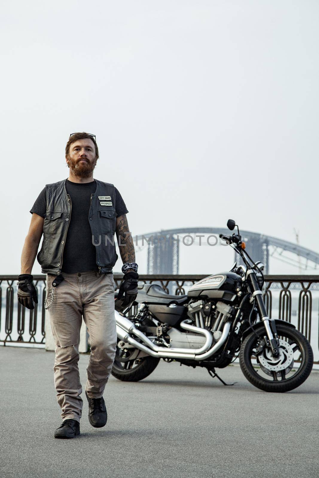 bearded motorcyclist man with his motorbike on summertime posing.