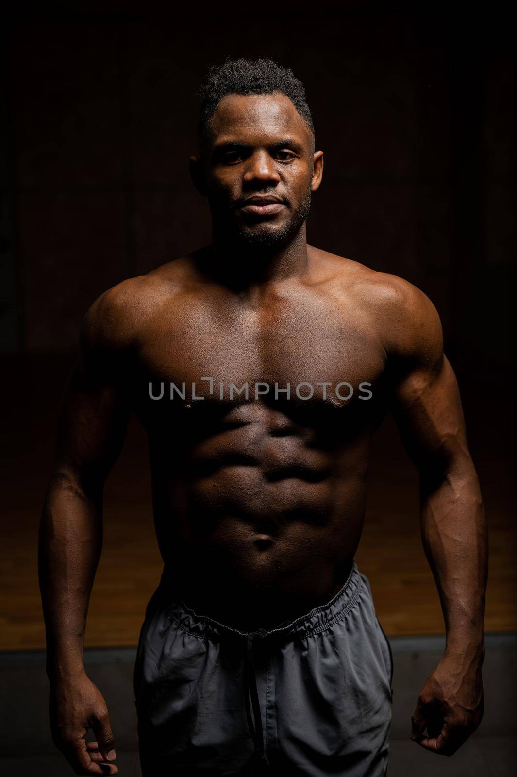 Portrait of an African American man with a naked torso in a dark studio. Muscular guy