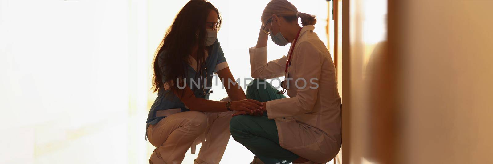 Low angle of tired medical worker after hard long surgery sitting on floor. Nurse support colleague doctor. Medicine, save life, health, tragedy concept