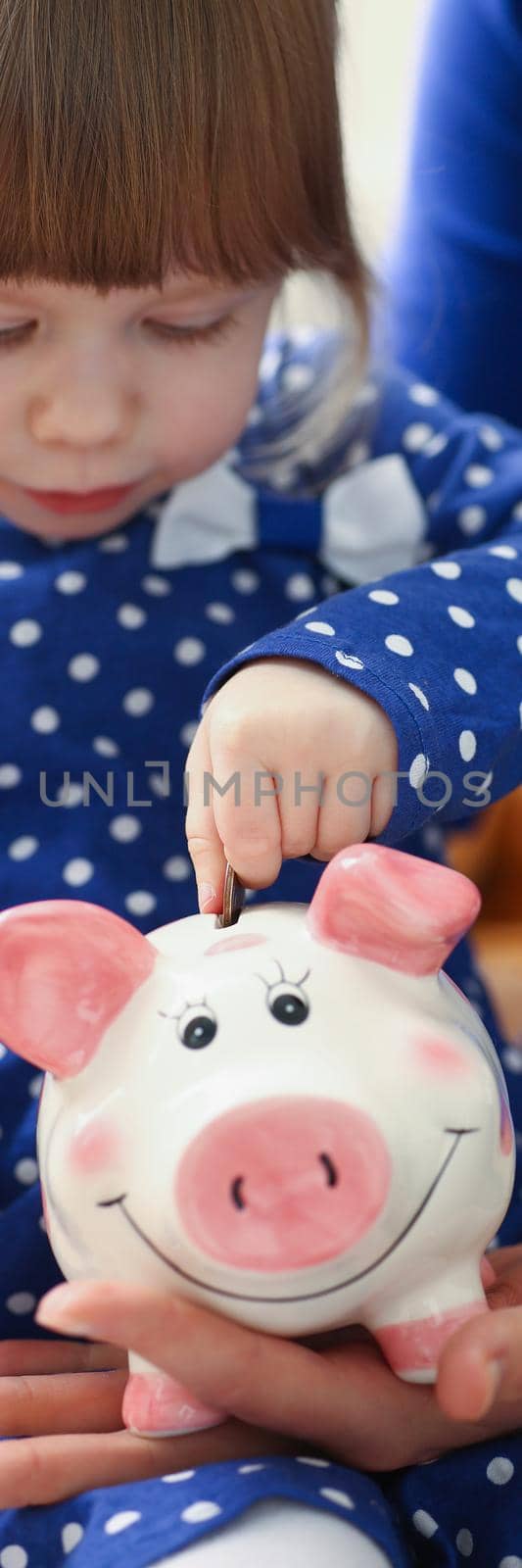 Portrait of cute little child putting coin cash into piggy bank container. Mother teach daughter to save up, save to buy toy. Childhood, investment concept