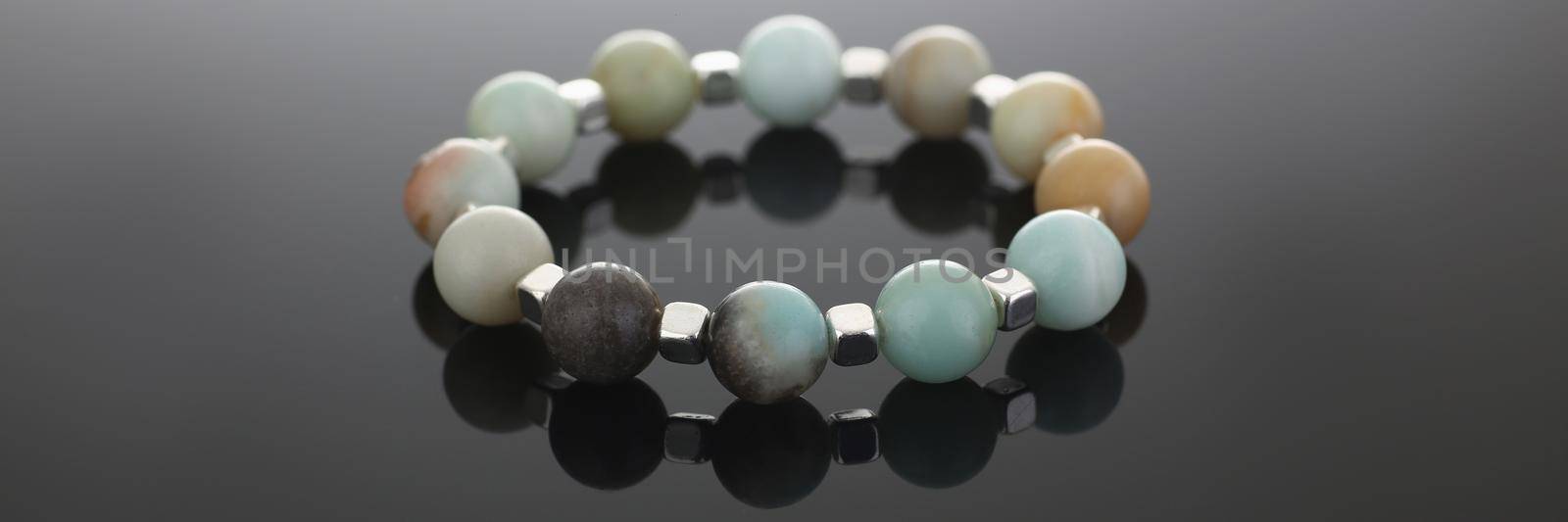 Close-up of shiny cute hand bracelet made of semiprecious stones. Real energy crystal presented on grey background with reflection. Heal, accessory concept