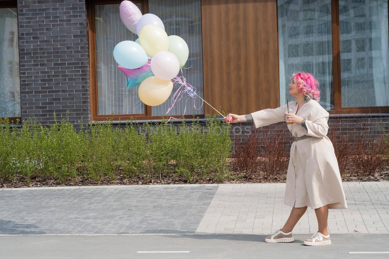 Woman in colored hair walks with an armful of balloons and drinks a refreshing beverage by mrwed54