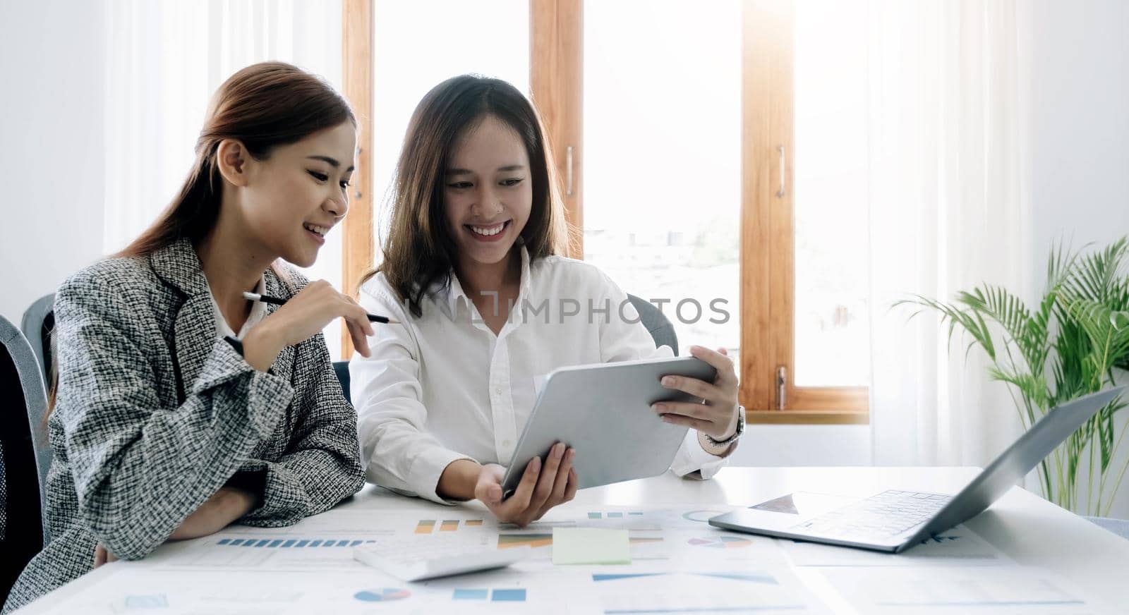 Two beautiful young asian businesswoman working together using digital tablet at office. by wichayada