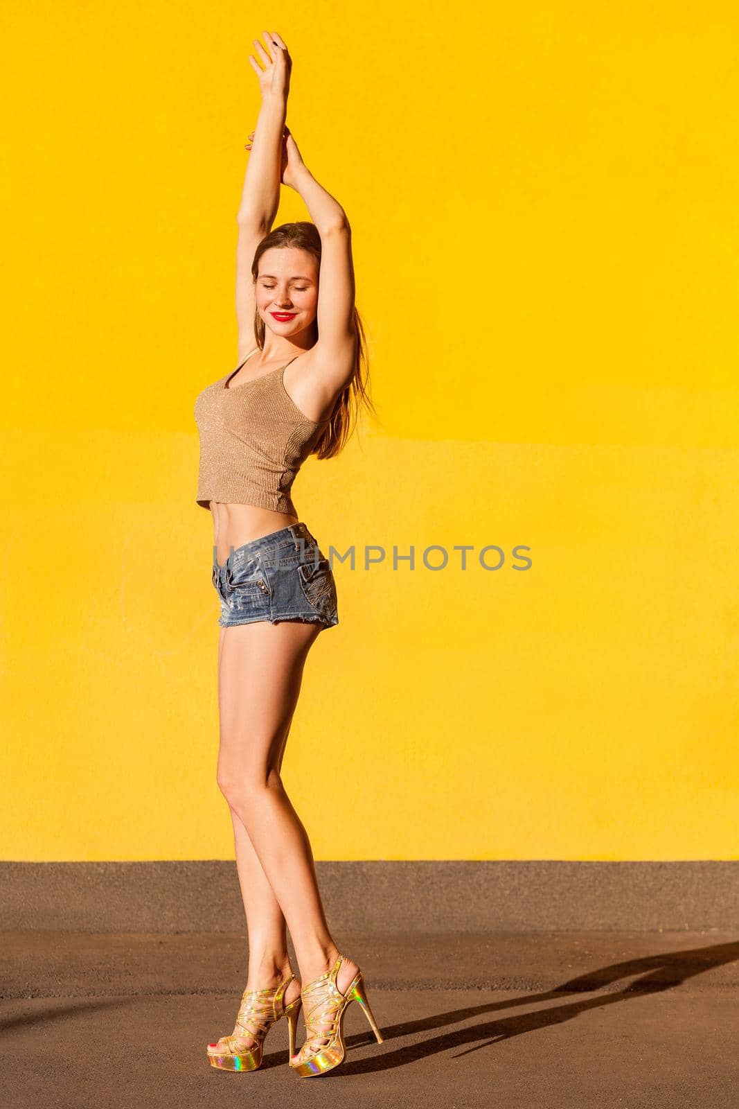 Very hot young freckled model beckoned you. Sensual brunette passionately closed eyes and hands up. Isolated on yellow background. Studio shot
