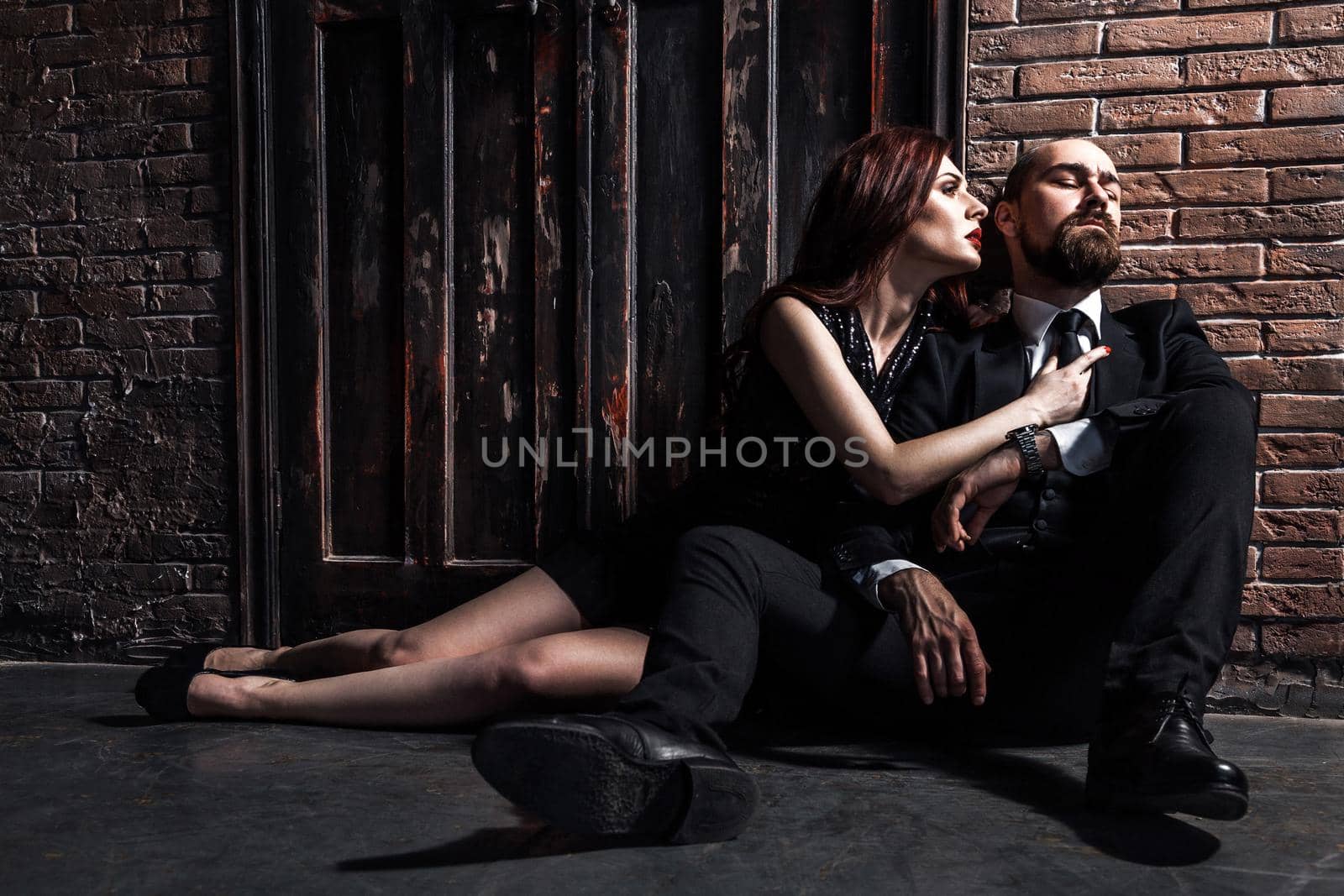 Businessman have a bad mood. Couple sitting on flor after quarrel. Ginger woman want kissing. Studio shot