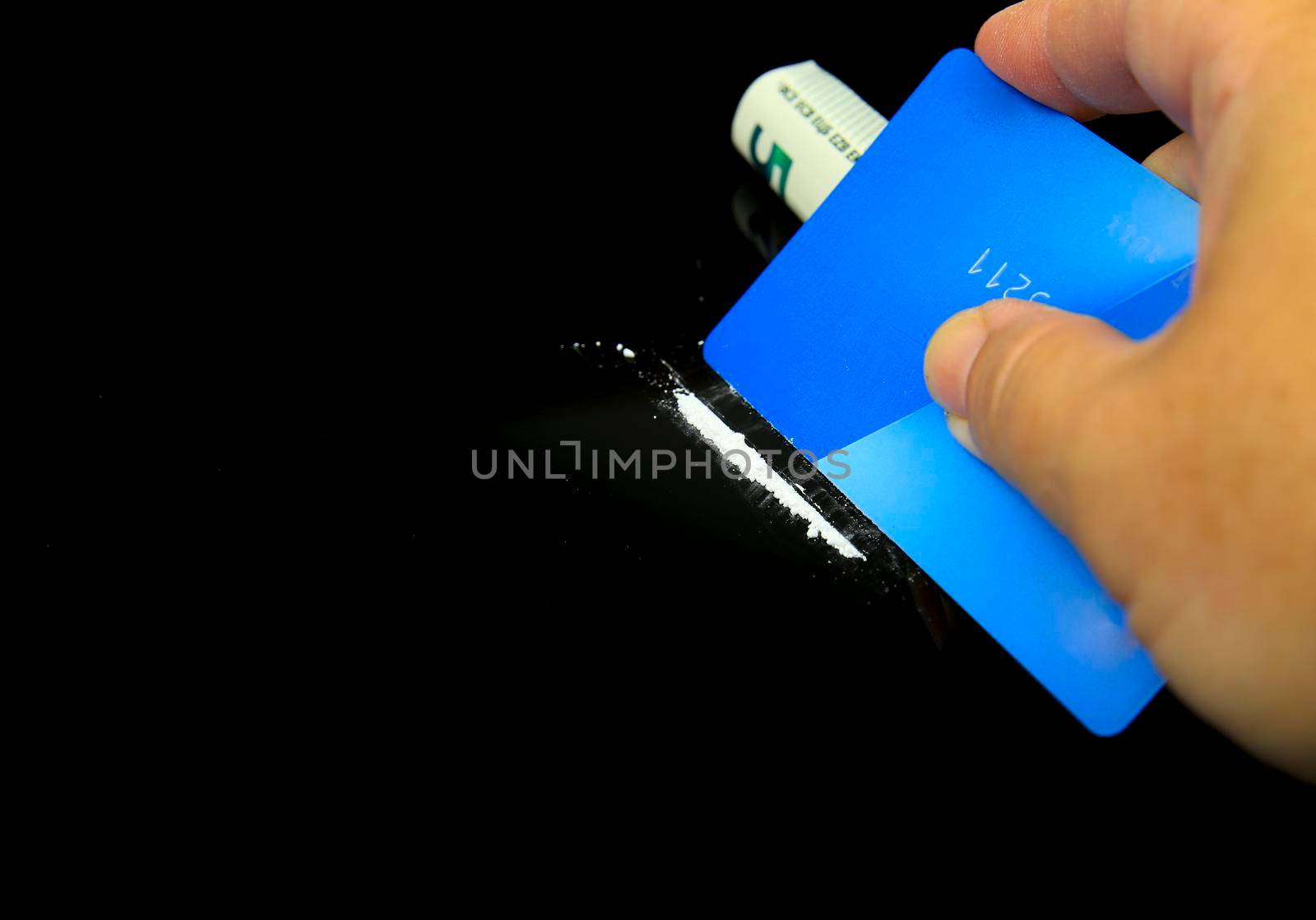 Hand with credit card making line of cocaine on black background