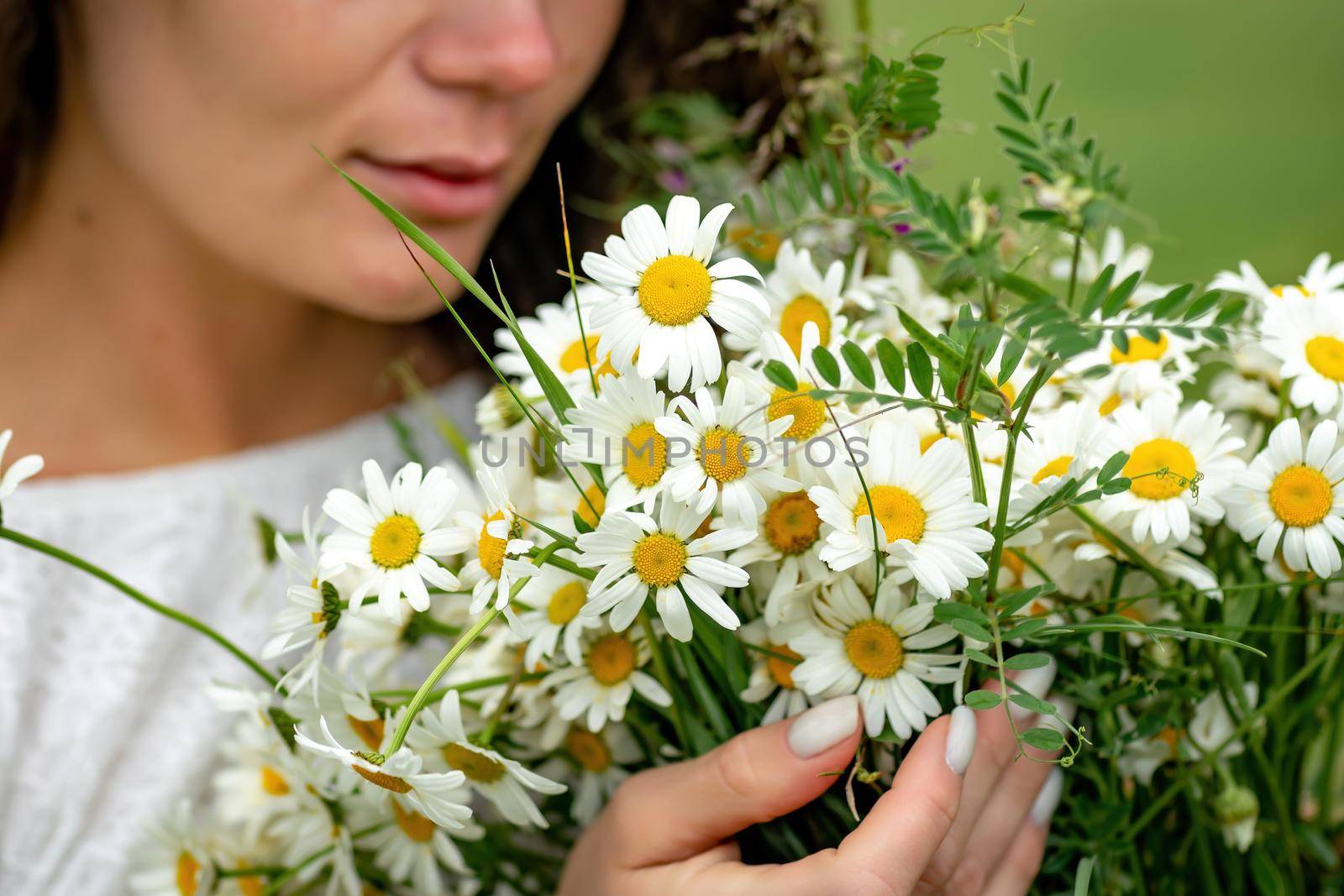 A middle-aged woman holds a large bouquet of daisies in her hands. Wildflowers for congratulations.