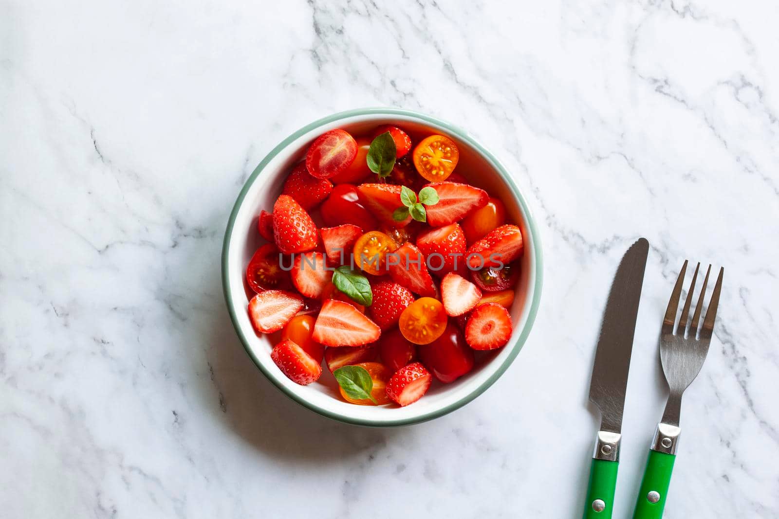 bowl of tomato cherry and strawberry mix salad on the marble background, top view