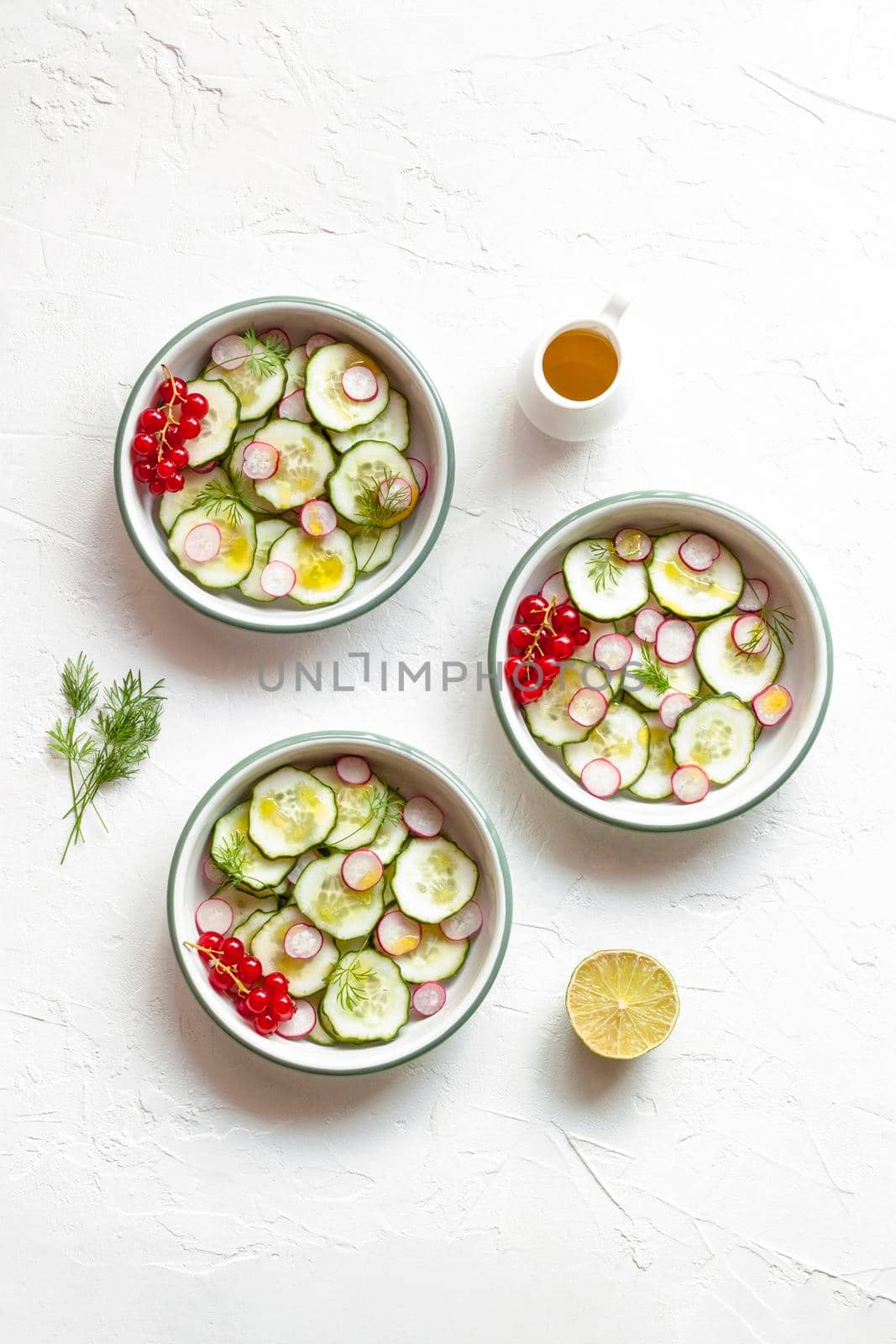radish and cucumber salad served in three round bowls decorated with red currants, white concrete background, top view