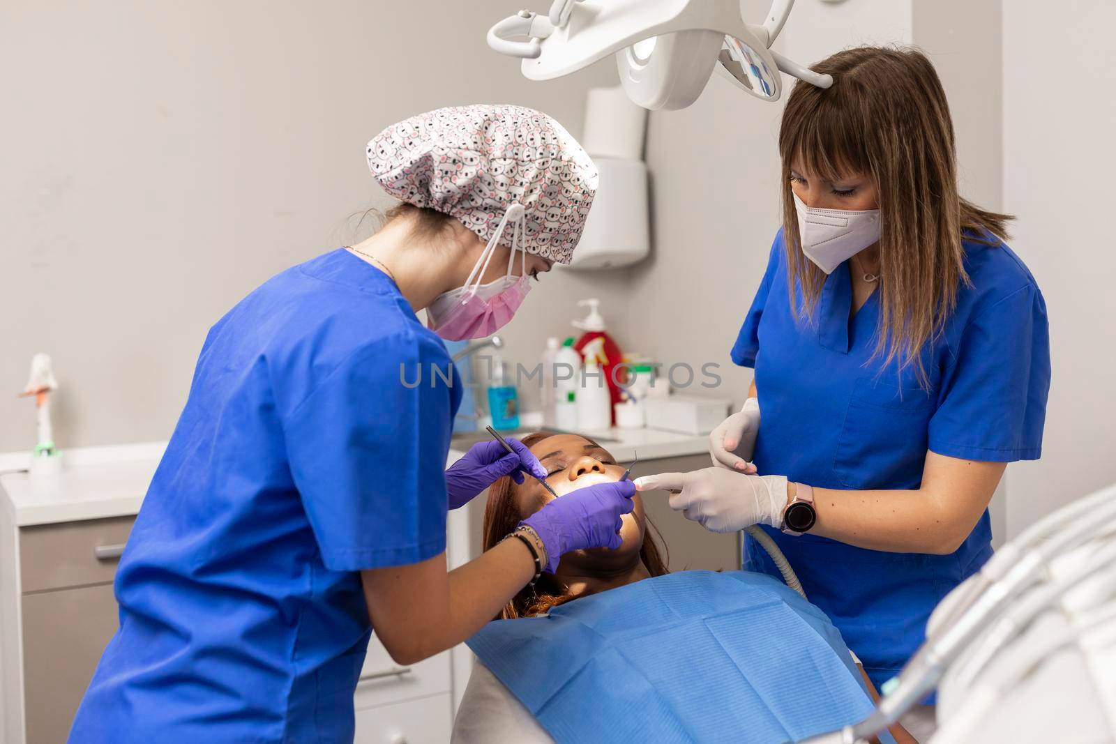 Two dentist women give dental treatment to a black race woman patient by stockrojoverdeyazul