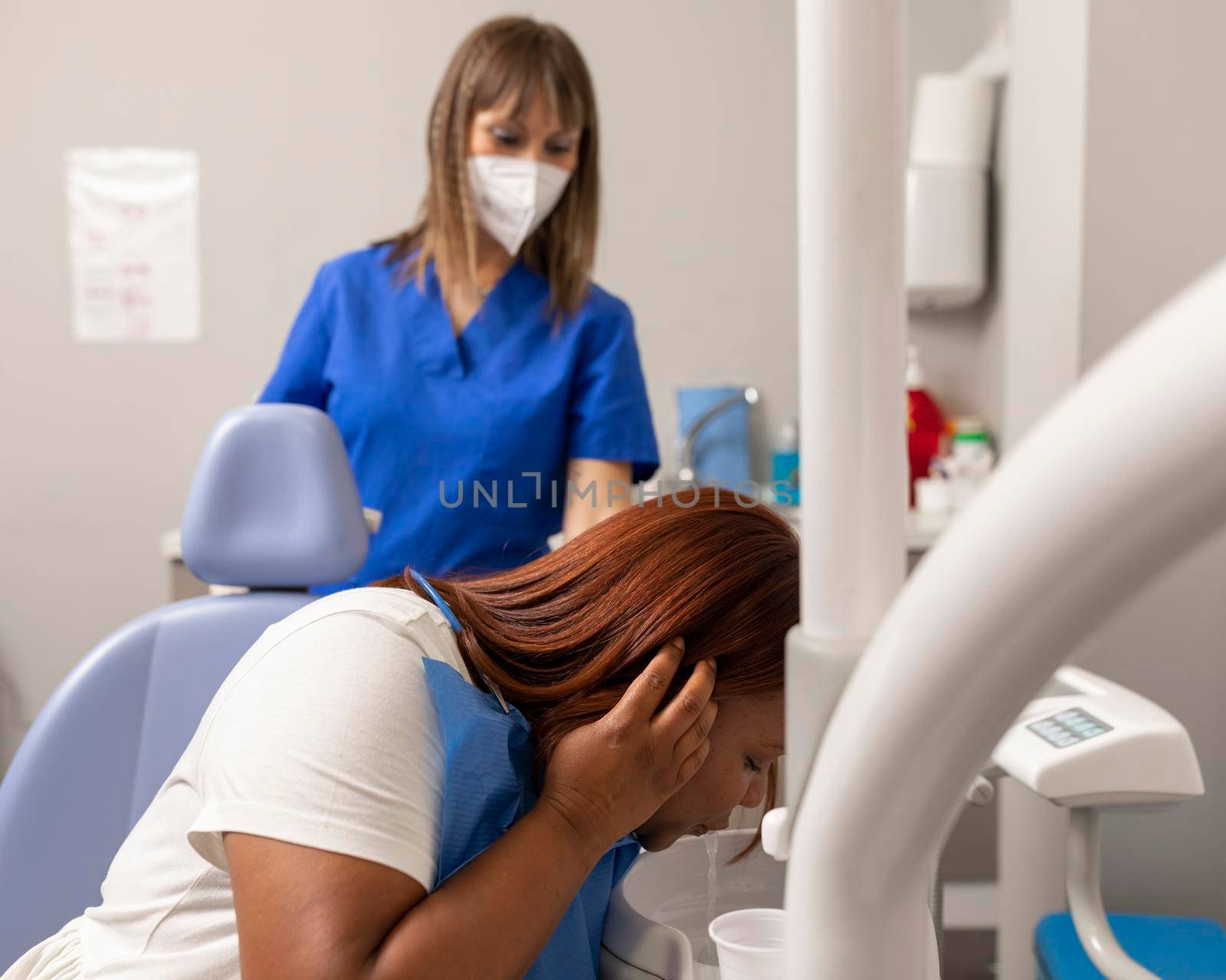 A black woman patient is spitting out after rinsing her mouth while waiting for the dentist to start the treatment at the dental clinic