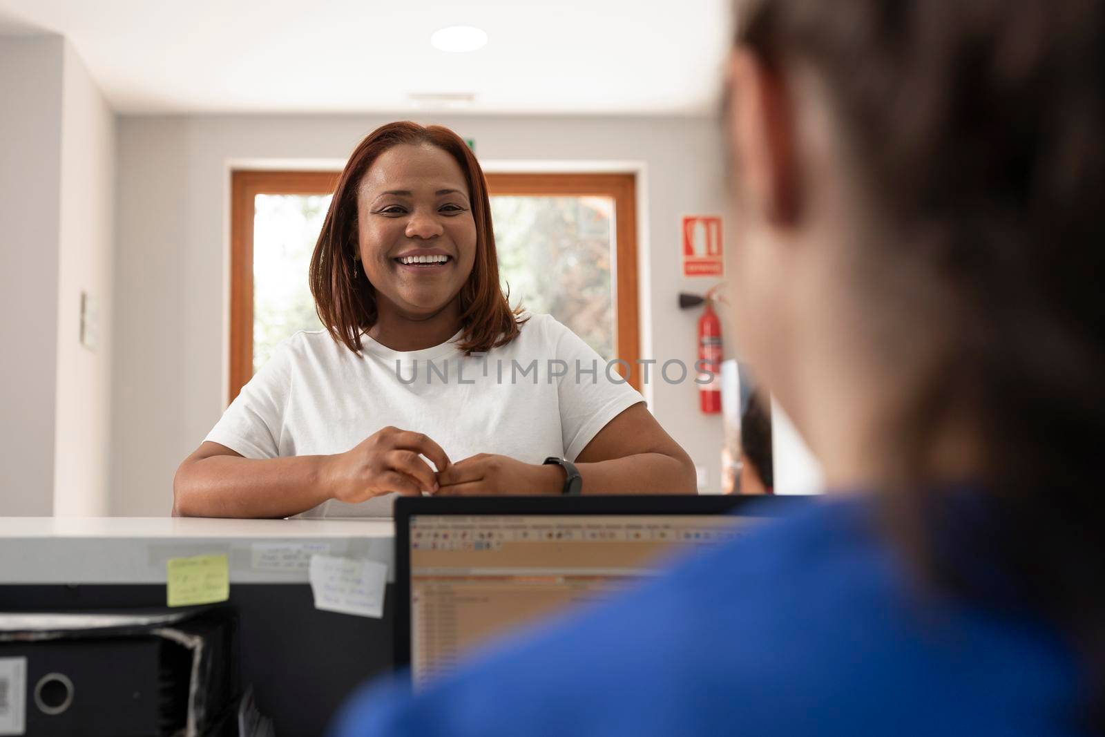 Black woman client talks with one of the employees at the dental clinic by stockrojoverdeyazul