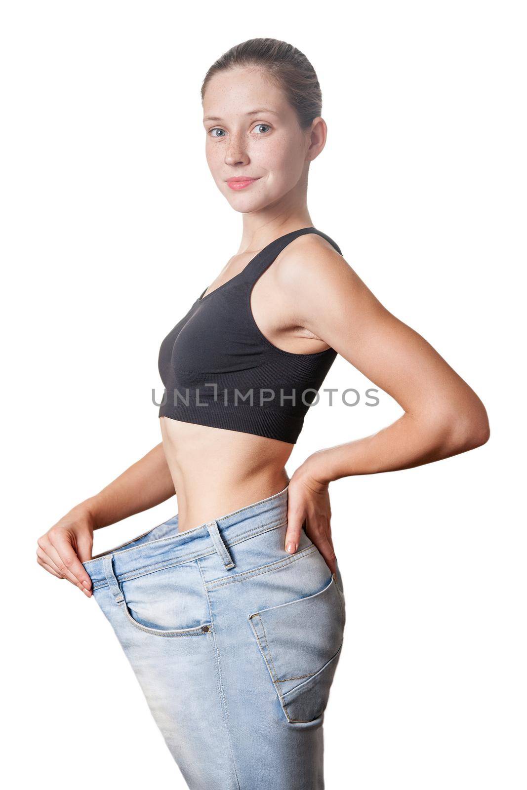 Close-up of slim waist of young woman in big jeans showing successful weight loss, isolated on white background, diet concept.