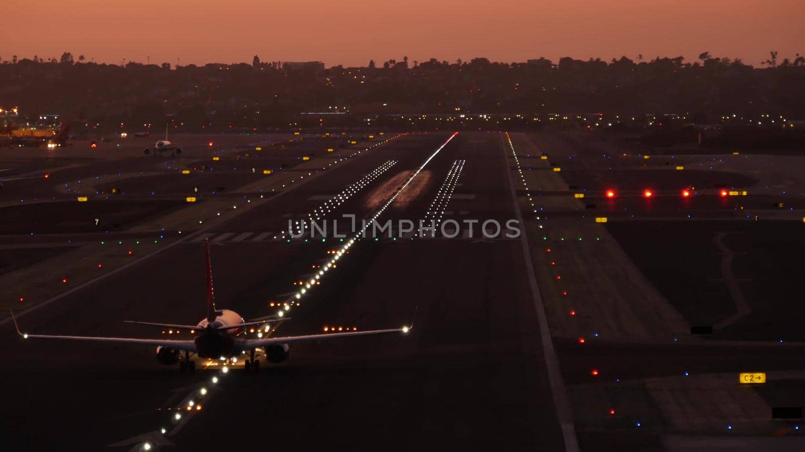 Airport runway lights at night, plane or airplane taking off from airstrip, twilight dusk after sunset. Aircraft or airliner jet departure from aerodrome, San Diego airfield in evening, California USA
