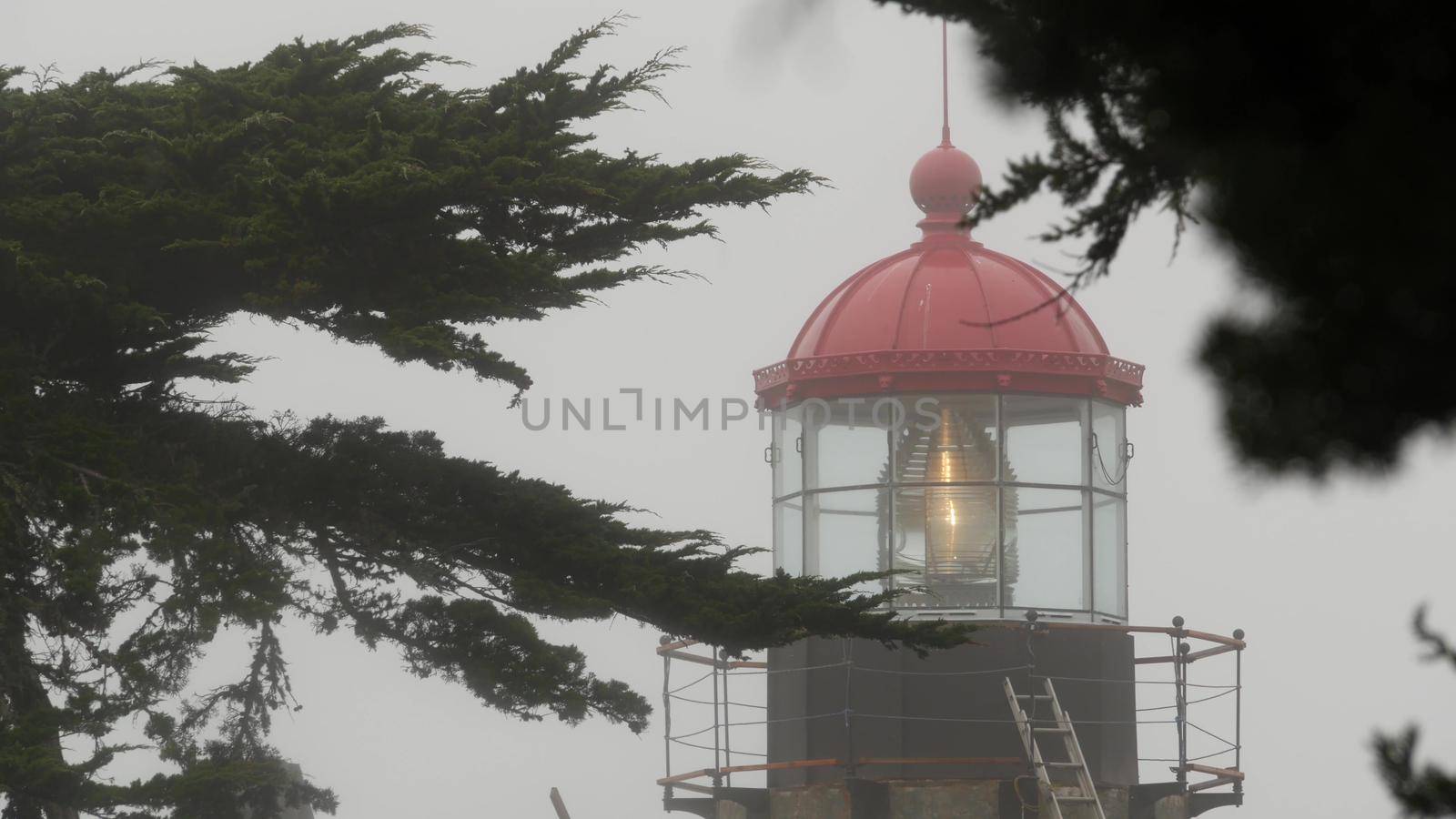 Old lighthouse fresnel lens glowing, foggy rainy weather. Illuminated beacon USA by DogoraSun