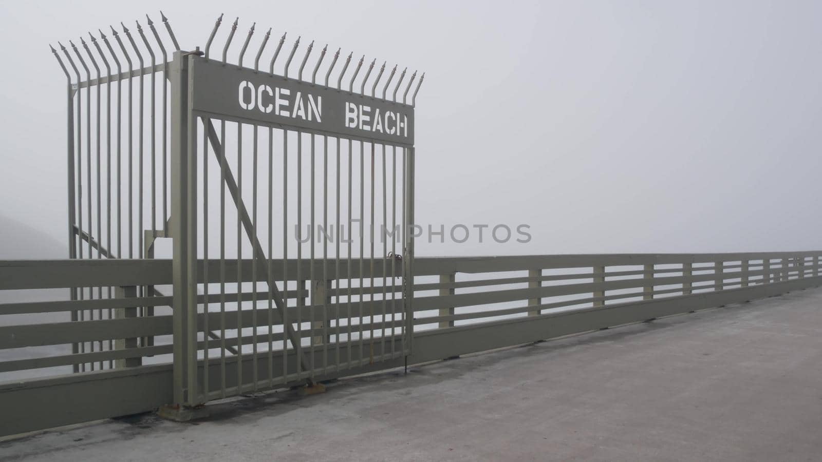 Metal gate on Ocean Beach pier in fog, misty California coast, USA. Foggy moody cloudy weather on San Diego shore. Calm tranquil atmosphere. Waterfront boardwalk entrance in gloomy depressive haze.