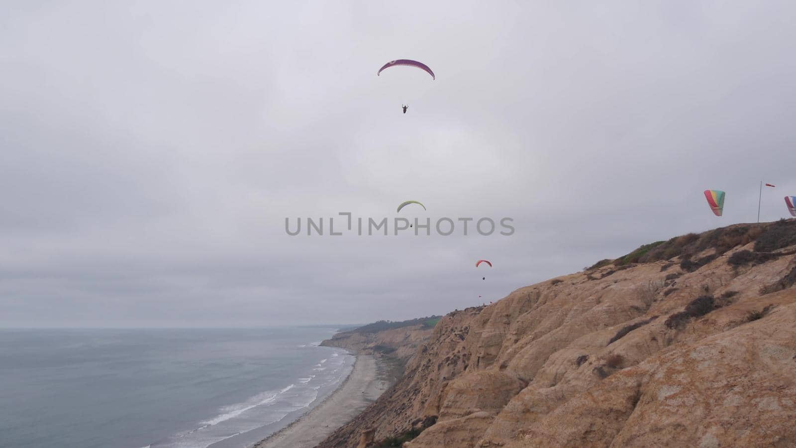 People paragliding, Torrey Pines cliff or bluff. Paraglider soaring in sky air, flying on parachute, kite or wing. Recreational sport hobby. Ocean coast, San Diego, California USA. Para gliding flight