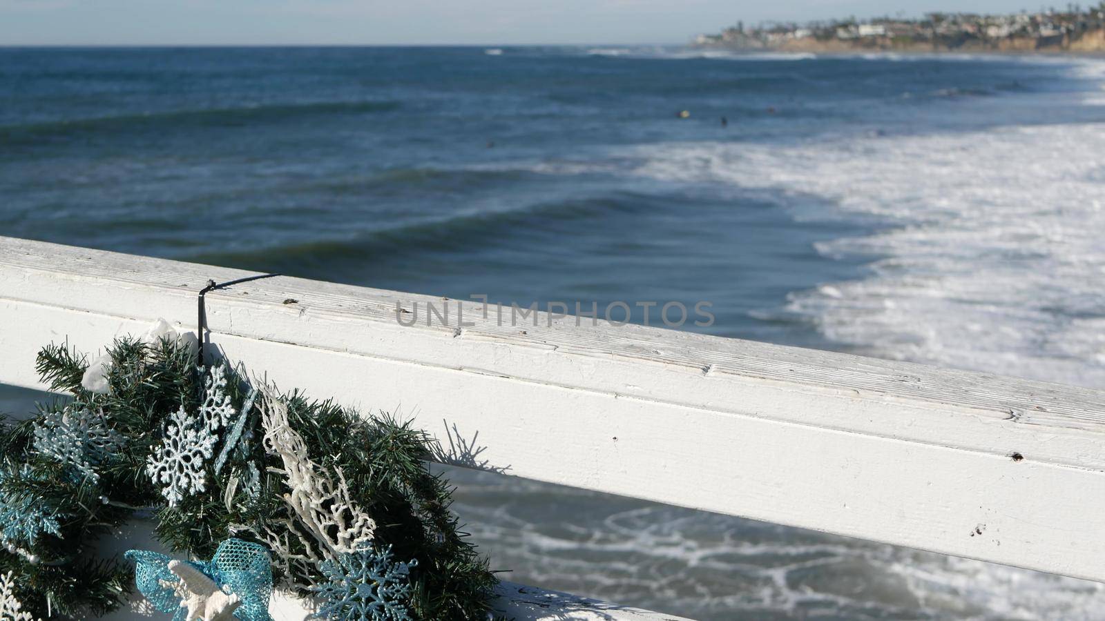 Christmas wreath on pier, New Year on ocean coast, California beach at Xmas. Decor from pine or fir tree for winter holidays over sea in USA. Festive decoration over summer seascape in December.