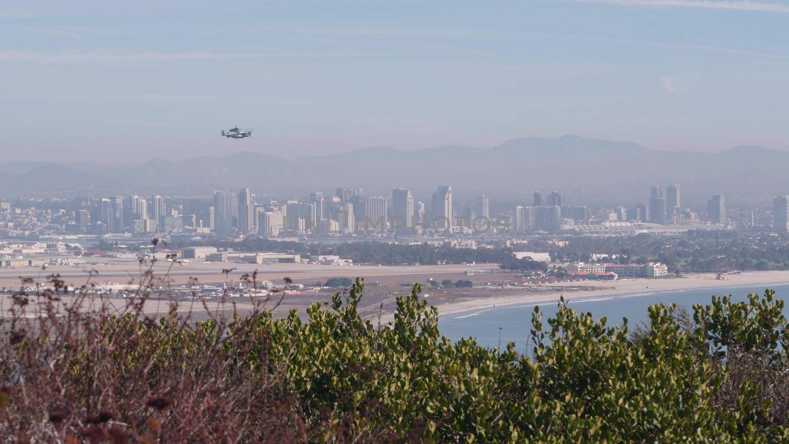 San Diego city skyline, cityscape of downtown with highrise skyscrapers, California coast, USA. View of Coronado island from above, Point Loma vista viewpoint. Helicopter flying mid air in sky.