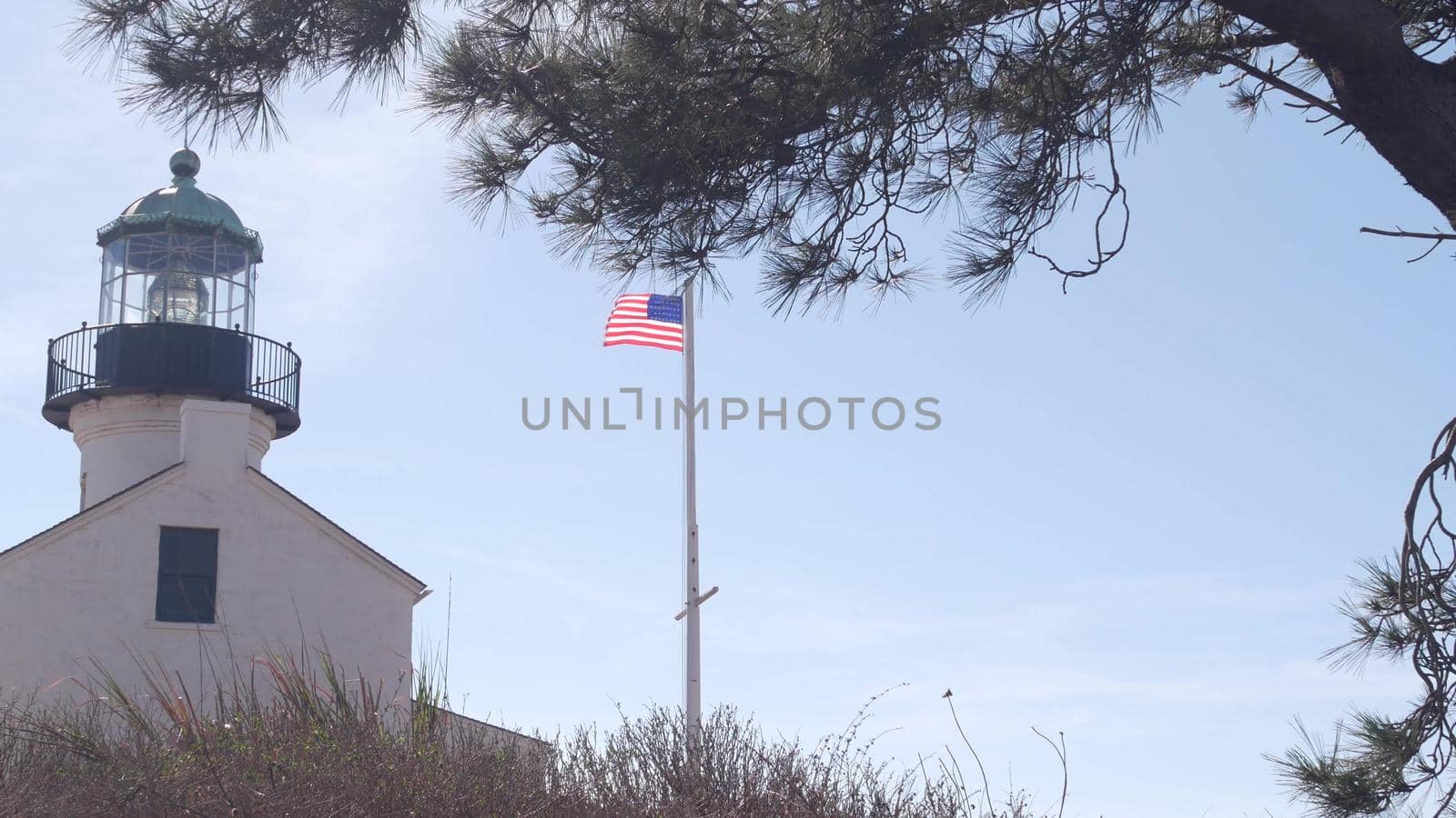 Vintage lighthouse tower, retro light house, old fashioned historic classic white beacon, fresnel lens, american flag. Nautical navigation, coastal building 1855. Point Loma, San Diego, California USA
