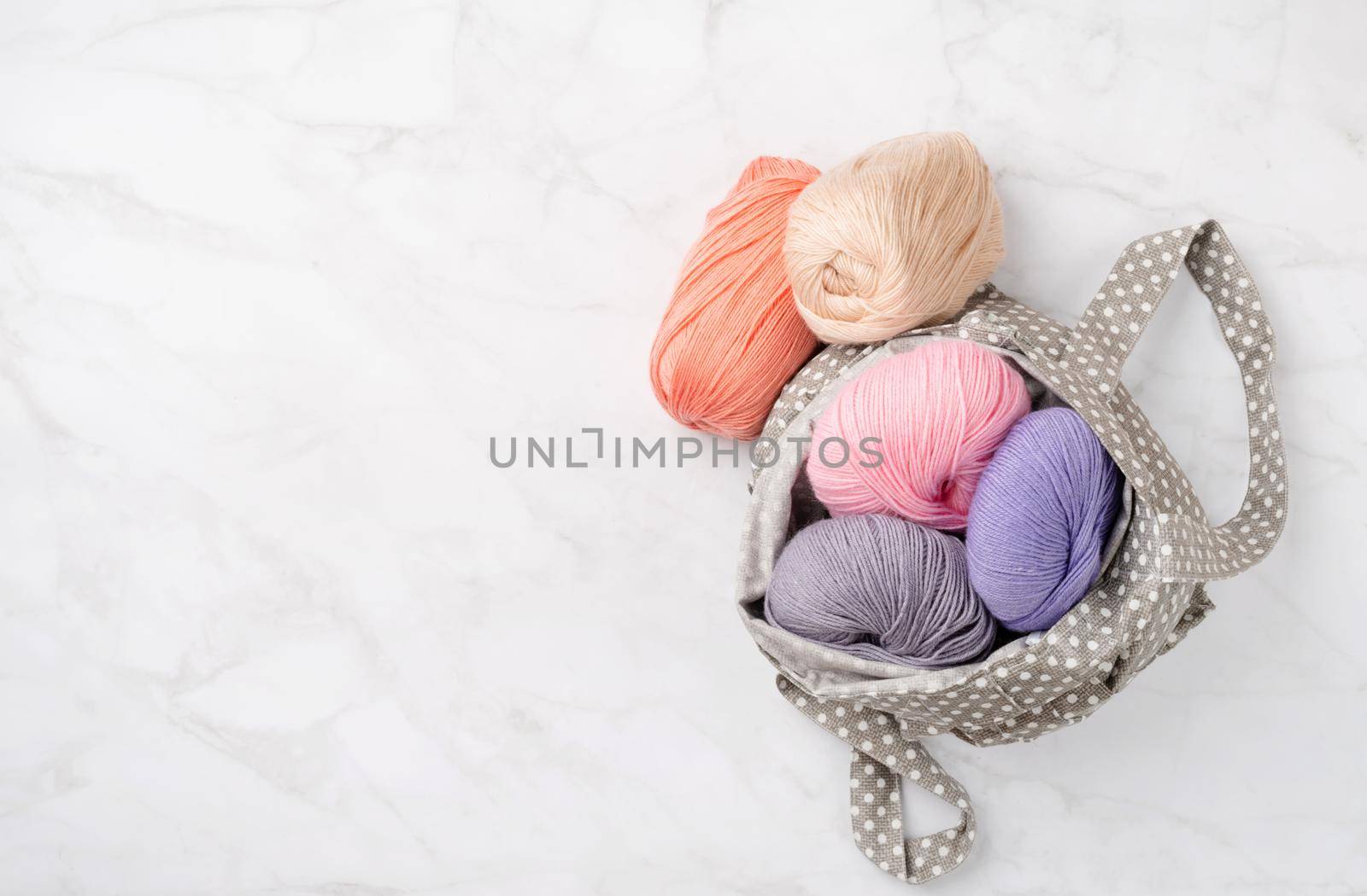 pastel colored yarn wool in a fabric shopping bag on marble background, top view. Hobbies and leisure. Eco friendly, zero waste