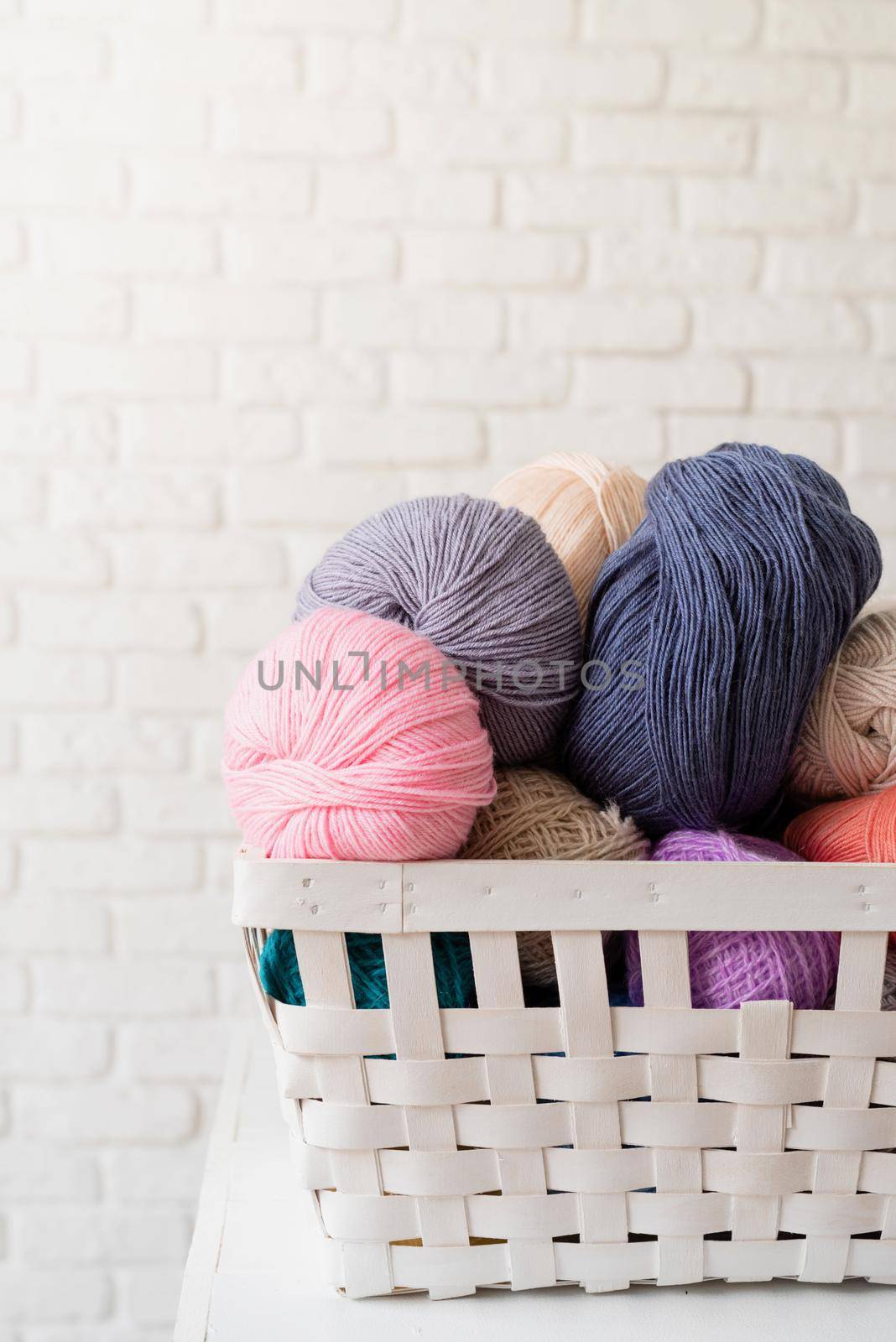 pastel colored yarn wool in a white basket on white brick wall background by Desperada
