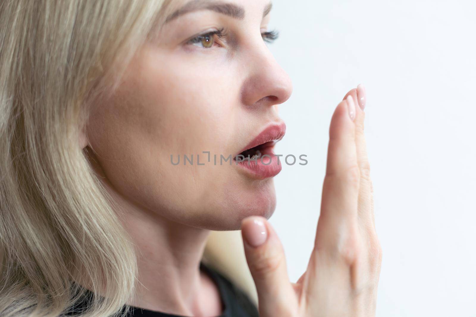 young girl checks her breath with her hand.